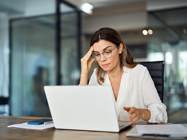 Business-Frau sitzt vor dem Laptop und stützt sichtlich gestresst ihren Kopf Business-Frau sitzt vor dem Laptop und stützt sichtlich gestresst ihren Kopf