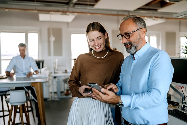 Mitarbeitende schauen im Büro auf ihre Smartphones, während sie im organisatorischen Austausch sind